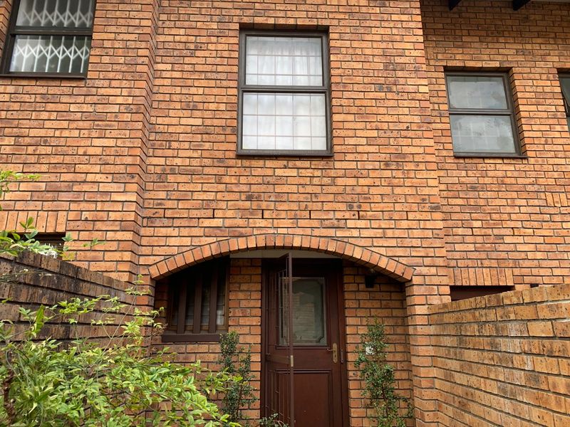 Front entrance of a face brick townhouse featuring an arched brick doorway, security-fitted windows, and a private brick boundary wall.