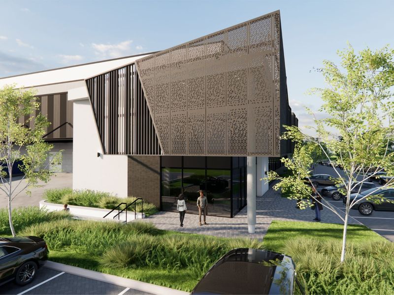 A modern industrial building exterior featuring a decorative metal screen facade, glass entrance, and landscaped parking area.