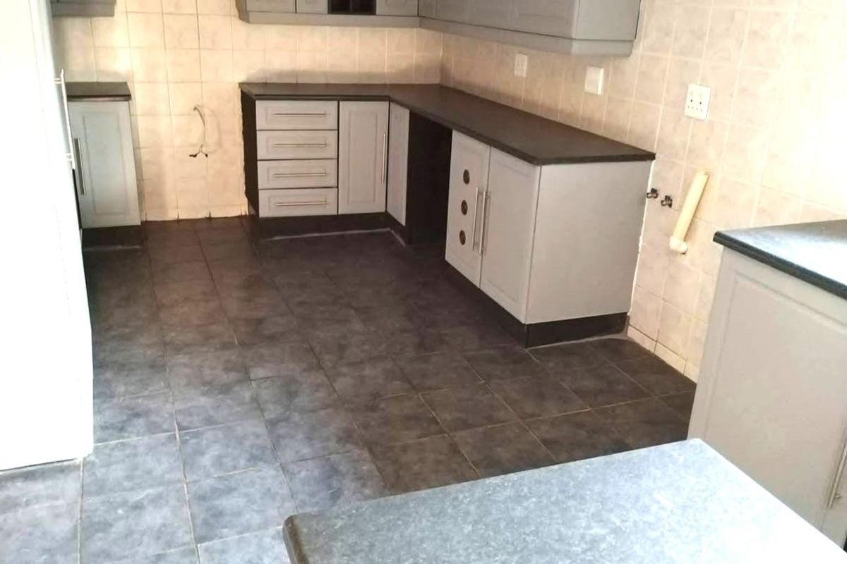 A functional kitchen space featuring grey cabinetry, dark laminate countertops, tiled splashbacks, and tiled flooring, currently vacant and ready for appliances.