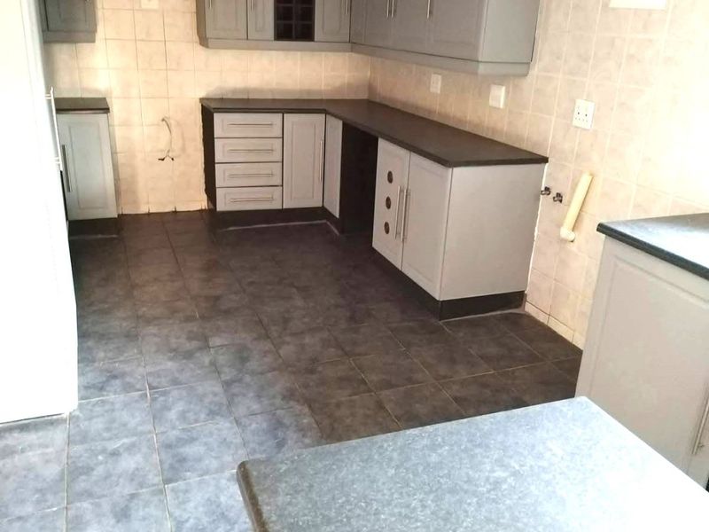 A functional kitchen space featuring grey cabinetry, dark laminate countertops, tiled splashbacks, and tiled flooring, currently vacant and ready for appliances.