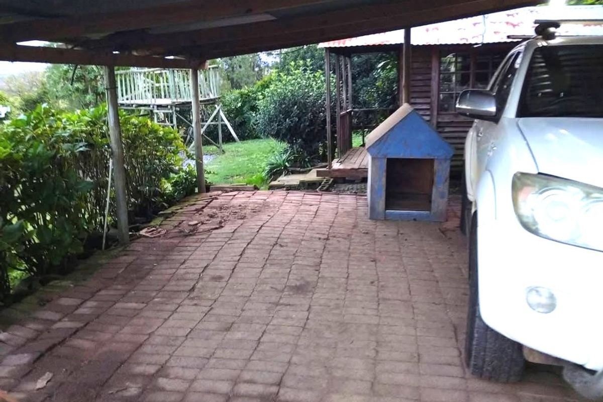 A covered outdoor patio area featuring brick paving and a timber roof structure, providing a functional space for vehicle parking or outdoor use.