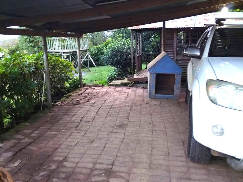 A covered outdoor patio area featuring brick paving and a timber roof structure, providing a functional space for vehicle parking or outdoor use.