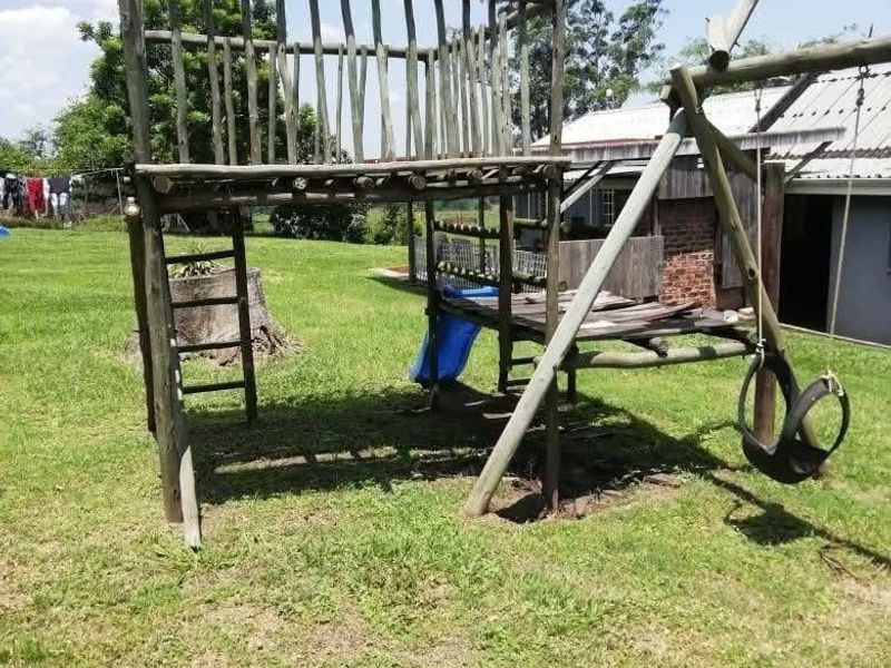 A large backyard area featuring a weathered wooden jungle gym and swing set structure set within a grassy lawn.