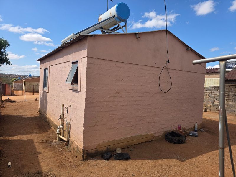 Rear view of a single-story house featuring exposed brick walls, a solar water heating system on the roof, and external plumbing fixtures.