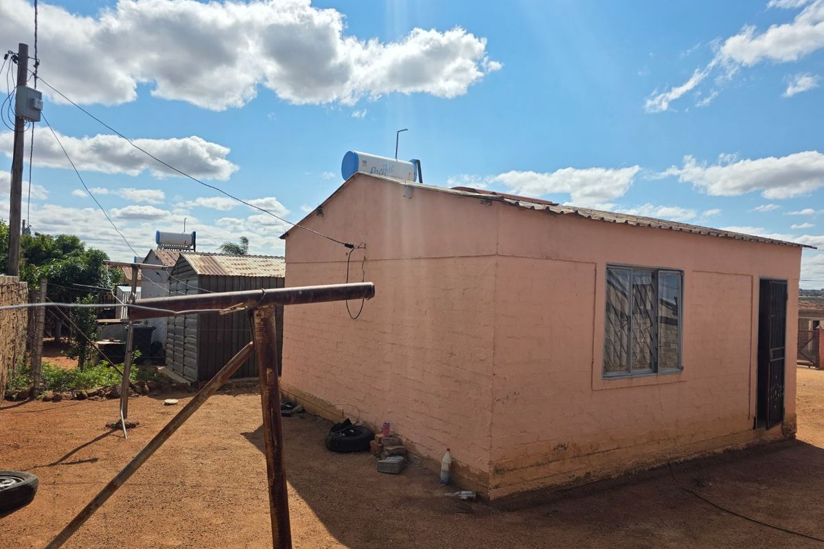 Rear view of a single-story residential dwelling featuring a solar water heater, metal roofing, and security bars on windows.