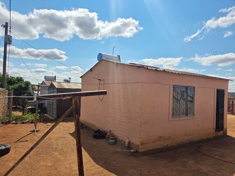 Rear view of a single-story residential dwelling featuring a solar water heater, metal roofing, and security bars on windows.