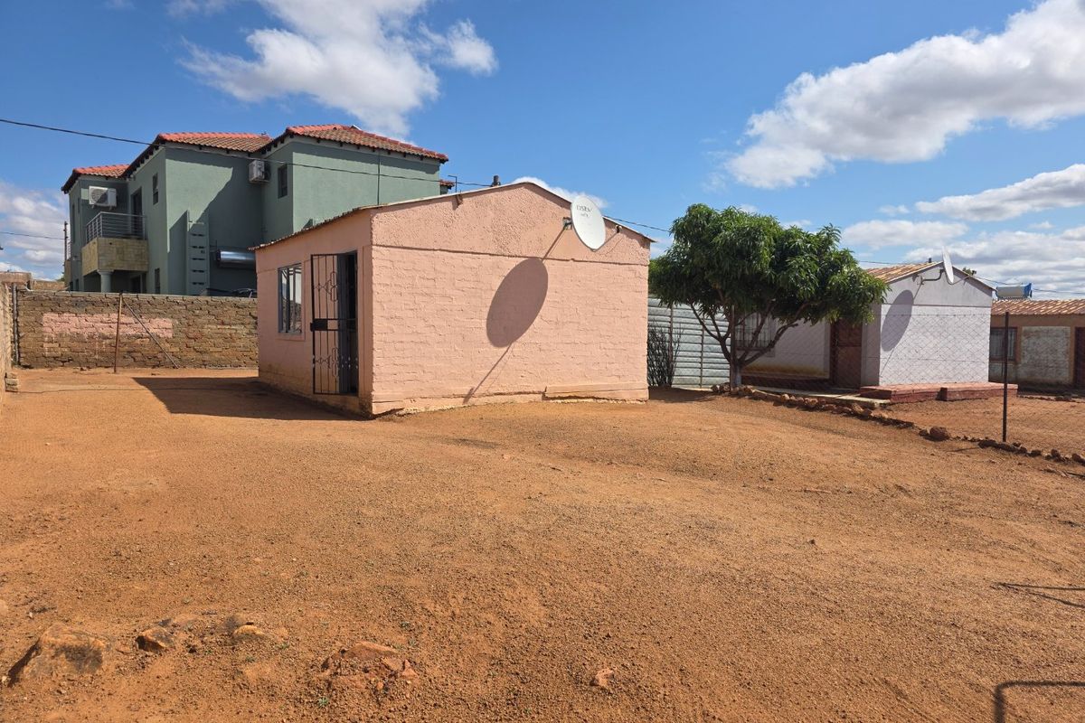 A view of the rear exterior area featuring a detached structure with a satellite dish and a large open dirt yard.