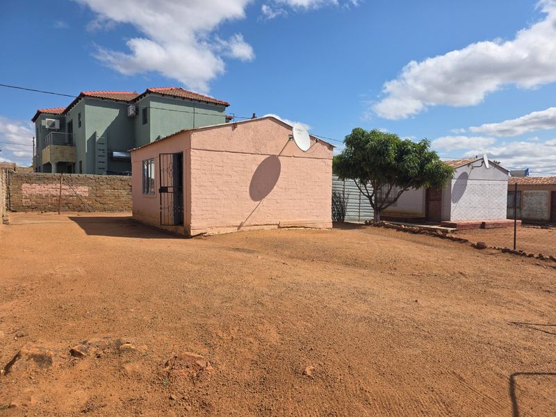 A view of the rear exterior area featuring a detached structure with a satellite dish and a large open dirt yard.