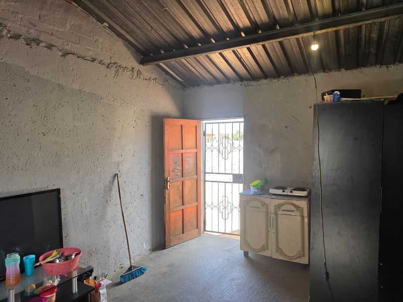 An open-plan living space featuring exposed rafters, corrugated metal roofing, and unfinished concrete walls, providing a basic shell ready for renovation.