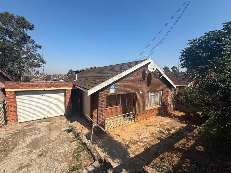 Front view of a face brick house featuring a single garage, concrete driveway, and tiled roof in a residential setting.