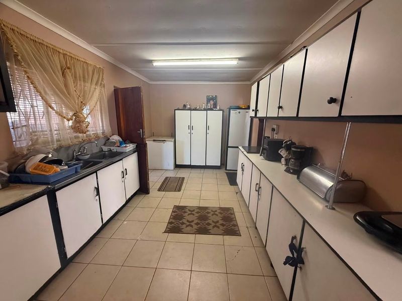 A functional kitchen featuring extensive built-in cabinetry, a double basin sink, and tiled flooring, offering a dated layout ready for modernization.