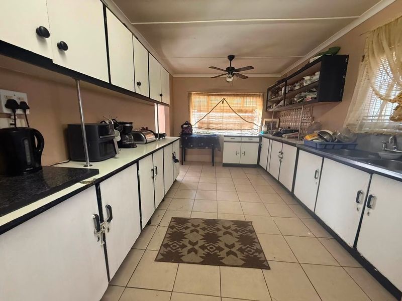 A functional kitchen featuring extensive built-in cabinetry, laminate countertops, a double sink, and tiled flooring, offering potential for a modern renovation.