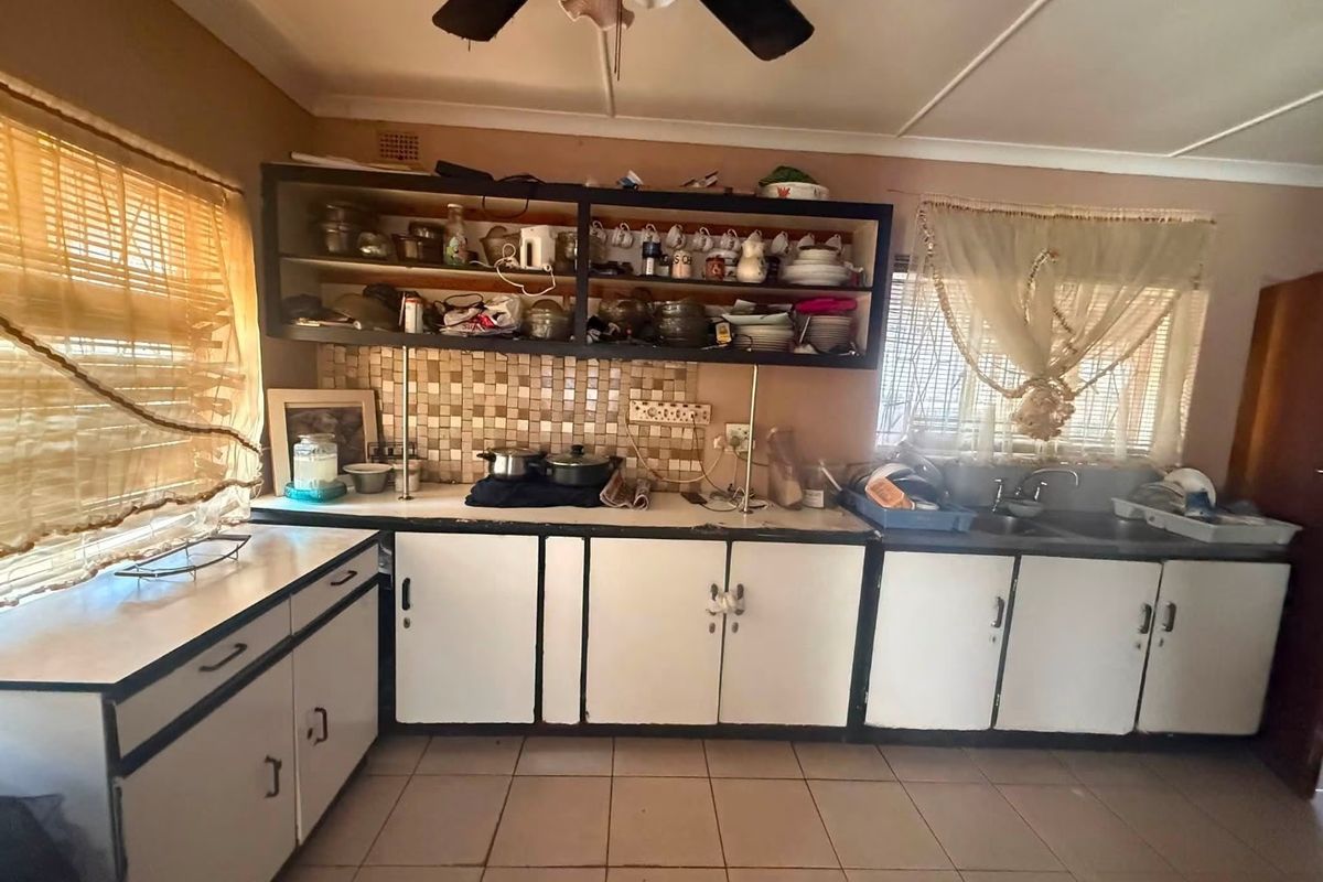 A dated kitchen featuring laminate cabinetry, mosaic tile backsplash, double basin sink, and tiled flooring, offering significant potential for modernization and renovation.