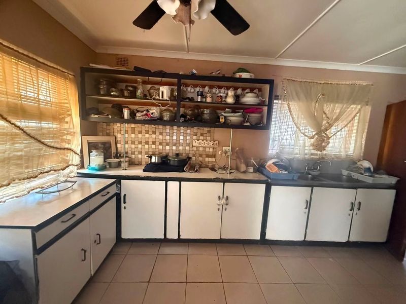 A dated kitchen featuring laminate cabinetry, mosaic tile backsplash, double basin sink, and tiled flooring, offering significant potential for modernization and renovation.