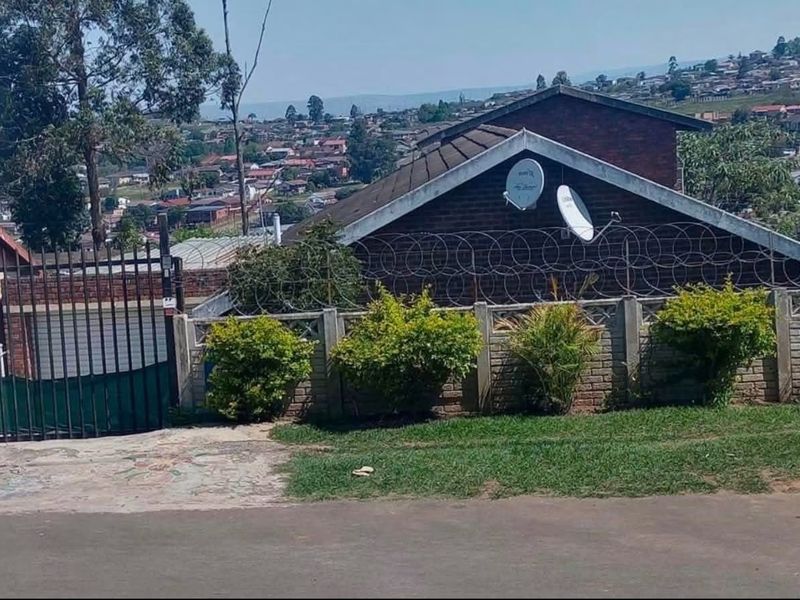 Front exterior view of the property featuring a brick facade, tiled roof, metal gate, and perimeter security fencing with razor wire.