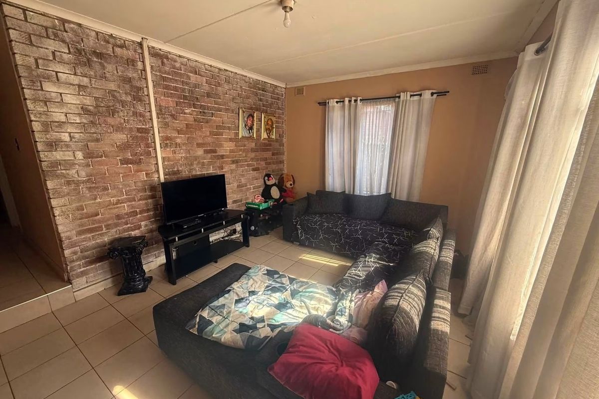 Living room featuring an exposed brick accent wall and tiled flooring, offering a functional space with potential for cosmetic updates.