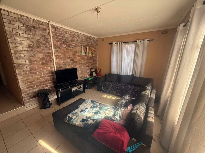Living room featuring an exposed brick accent wall and tiled flooring, offering a functional space with potential for cosmetic updates.