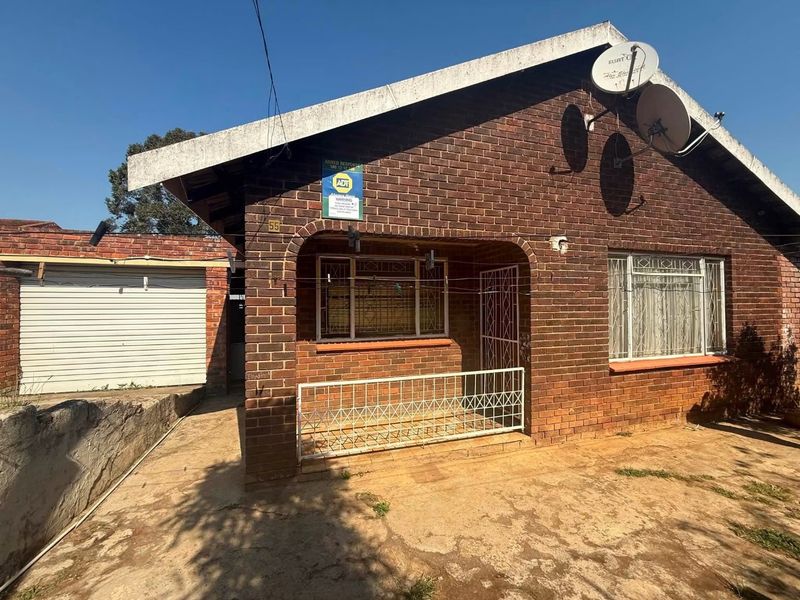 Front exterior view of a face brick house featuring a small covered porch, security gates, and an adjacent garage.
