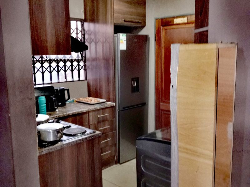 A compact kitchen featuring dark wood-finish cabinetry, stone-look countertops, and a built-in hob, providing a functional workspace with direct access to the home.