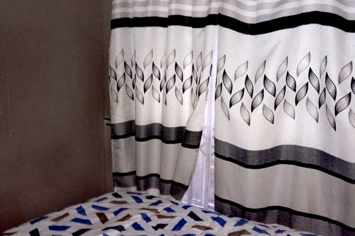 A bedroom interior featuring a window with a security gate and curtain rail.