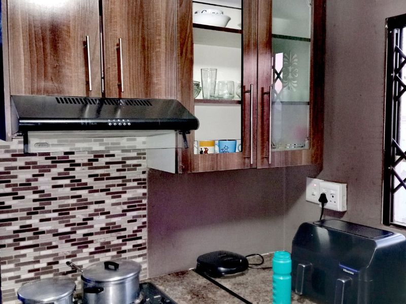 Compact kitchen featuring wood-look laminate cabinetry, a mosaic tile backsplash, electric hob with extractor fan, and integrated oven.