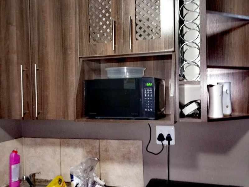 A functional laundry area featuring wood-finish built-in cabinetry, a stainless steel sink, tiled splashback, and dedicated space for a washing machine.
