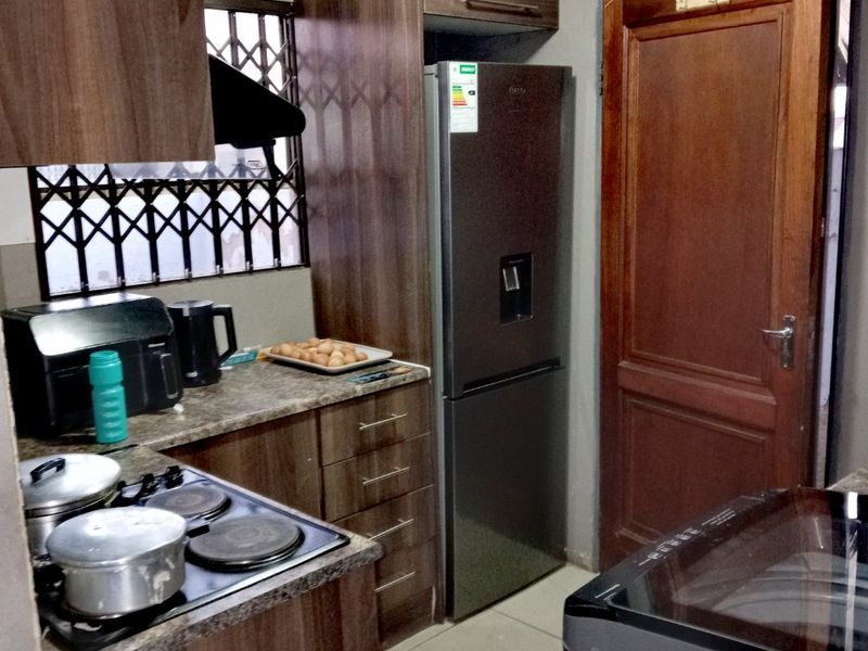 A functional kitchen featuring dark wood-look cabinetry, laminate countertops, a built-in electric hob, and tiled flooring with a secure window and timber door.