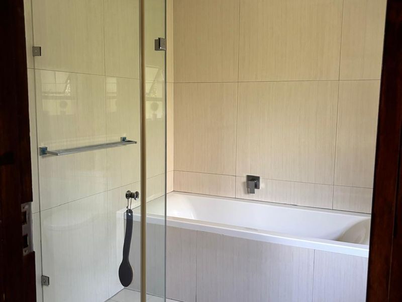 Modern bathroom featuring a built-in bathtub, a glass-enclosed shower, and neutral floor-to-ceiling wall tiles.