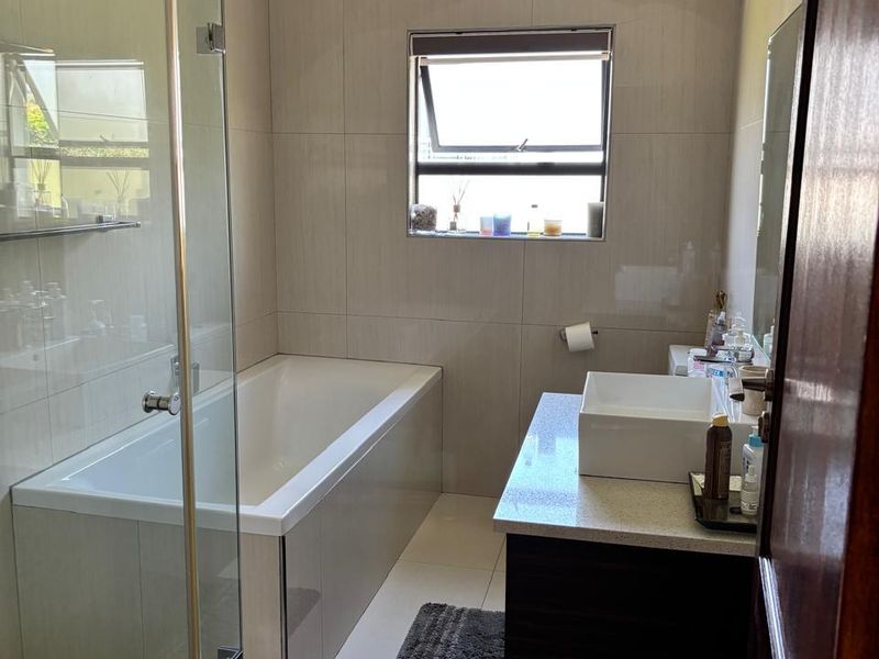 Modern bathroom featuring a built-in bathtub, glass-enclosed shower, and a vanity with a vessel sink and stone countertop.