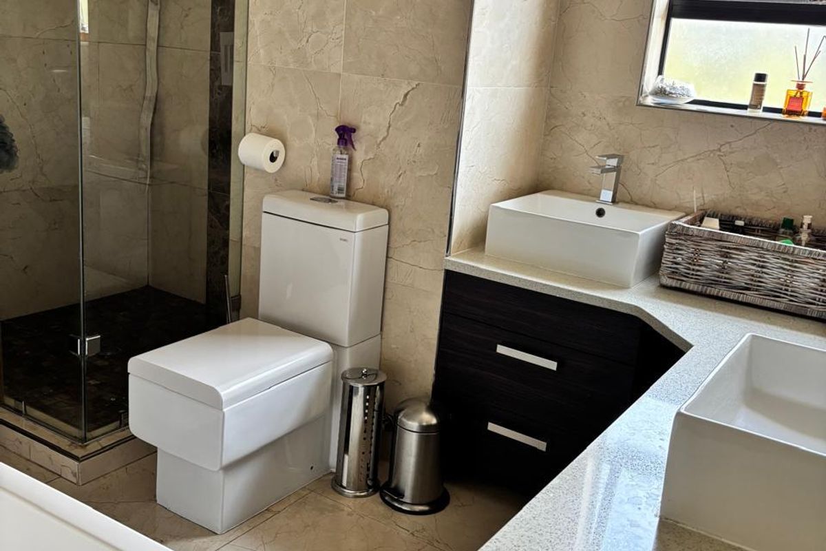 Modern bathroom featuring a double vanity with stone countertops, vessel sinks, a glass-enclosed rain shower, and floor-to-ceiling tiled finishes.