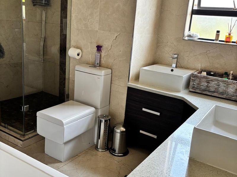 Modern bathroom featuring a double vanity with stone countertops, vessel sinks, a glass-enclosed rain shower, and floor-to-ceiling tiled finishes.