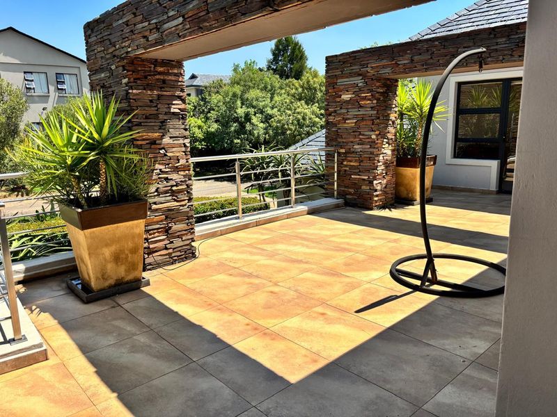 A spacious outdoor balcony featuring decorative stacked stone pillars, stainless steel railings, and durable tiled flooring, offering a pleasant elevated view.