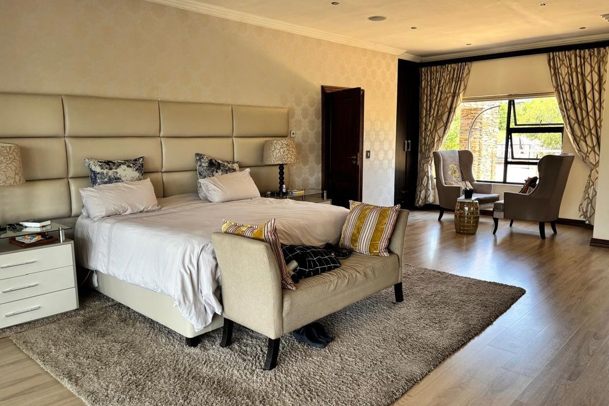 Spacious bedroom featuring laminate flooring, recessed lighting, built-in cupboards, and a large upholstered headboard with a cozy seating area by the window.