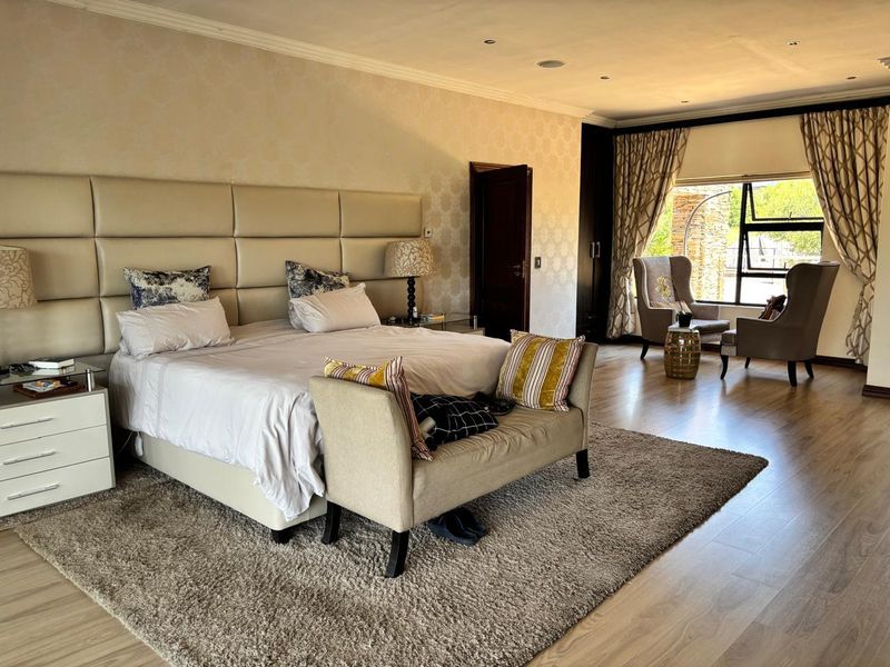 Spacious bedroom featuring laminate flooring, recessed lighting, built-in cupboards, and a large upholstered headboard with a cozy seating area by the window.