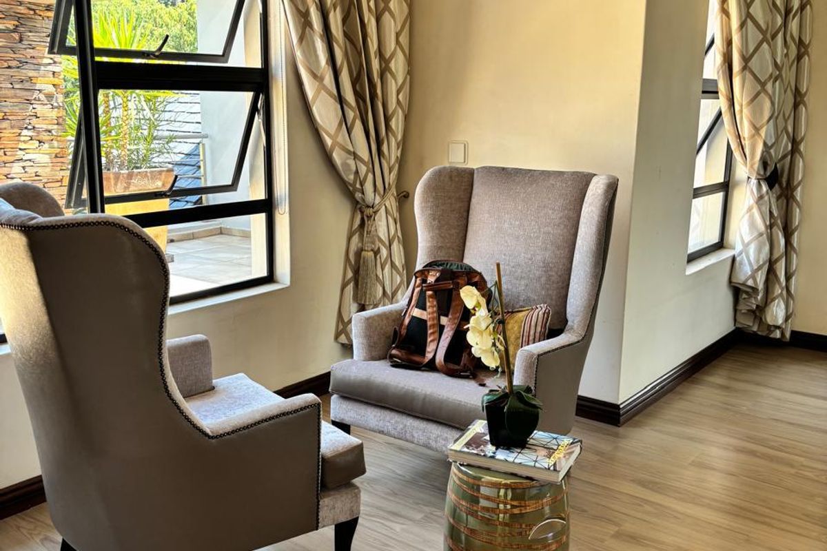 A bright living area featuring modern laminate flooring, neutral walls, and large windows with aluminium frames, creating a comfortable and well-lit space.