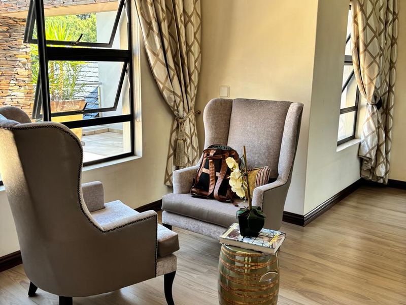 A bright living area featuring modern laminate flooring, neutral walls, and large windows with aluminium frames, creating a comfortable and well-lit space.