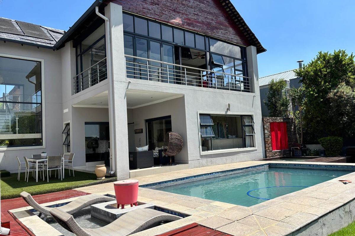 Rear exterior view of a two-story house featuring a swimming pool, wooden decking, a balcony, and large glass windows.