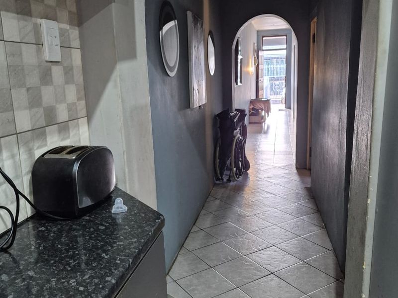 A hallway featuring arched architectural details, tiled flooring, and a transition area into the kitchen with granite countertops and tiled backsplash.
