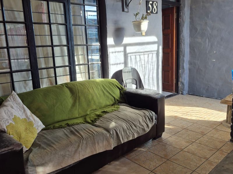 A covered patio area featuring tiled flooring, security window bars, and exterior wall lighting, providing a functional outdoor space for the home.