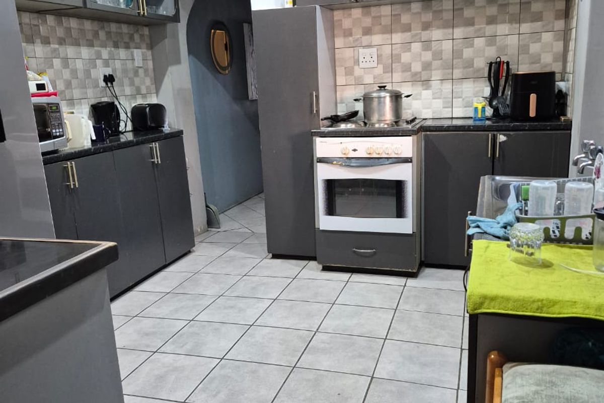 A functional kitchen featuring dark grey cabinetry, tiled backsplash, tiled flooring, and a freestanding oven with an integrated extractor fan.
