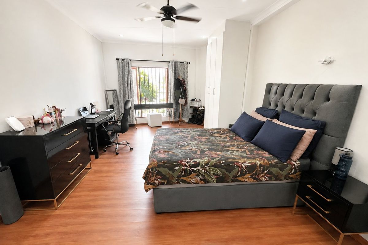 Spacious bedroom featuring laminate flooring, built-in cupboards, a ceiling fan, and recessed lighting, with security bars on the window.