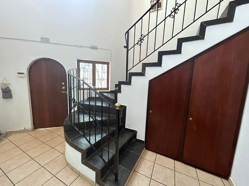 Spacious entrance hall featuring a distinctive curved tiled staircase with wrought iron railings and convenient under-stair storage cabinetry.