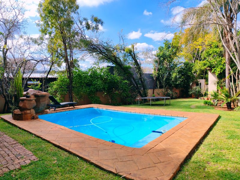 A well-maintained outdoor pool area featuring a rock water feature, paved surround, and established garden setting.