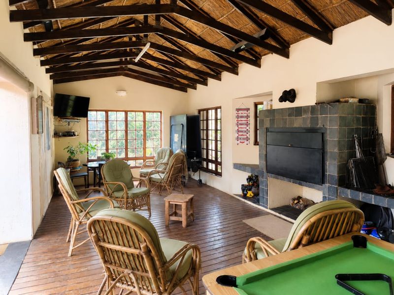 Spacious covered patio featuring exposed timber roof trusses, a thatched ceiling, timber decking, and a large built-in tiled fireplace.