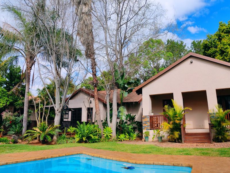 A well-maintained outdoor area featuring a swimming pool, covered patio with timber decking, and stone-clad accents set within a lush garden.