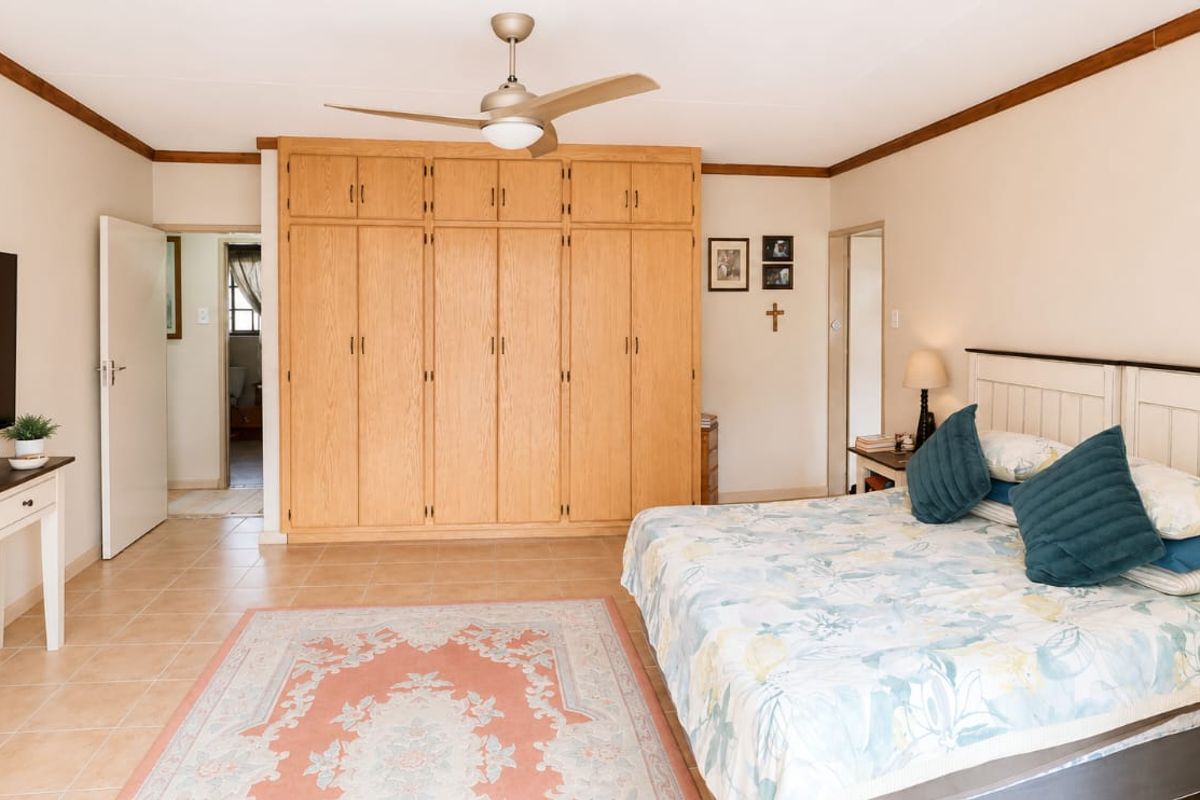 Spacious bedroom featuring extensive built-in wooden cabinetry, tiled flooring, and a ceiling fan, offering a functional layout with direct access to an adjoining room.