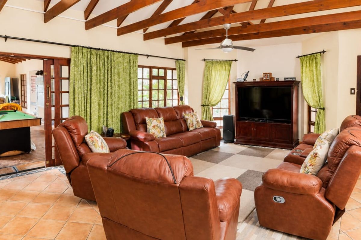 Spacious living room featuring exposed timber rafters, tiled flooring, and large timber-framed glass doors leading to an adjacent games area.