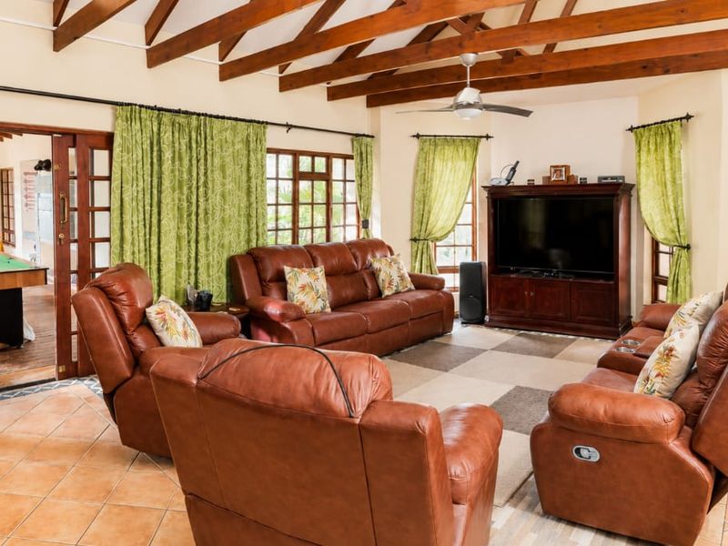 Spacious living room featuring exposed timber rafters, tiled flooring, and large timber-framed glass doors leading to an adjacent games area.