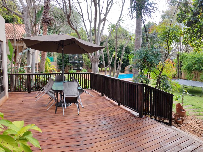 A spacious elevated timber deck featuring a balustrade, overlooking a lush garden and swimming pool area.
