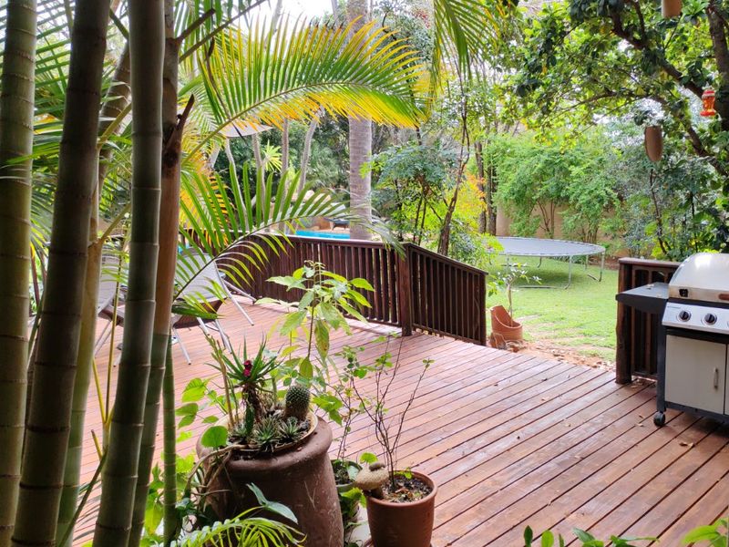 A wooden deck patio area overlooking a lush garden, featuring timber balustrades and a natural outdoor setting.